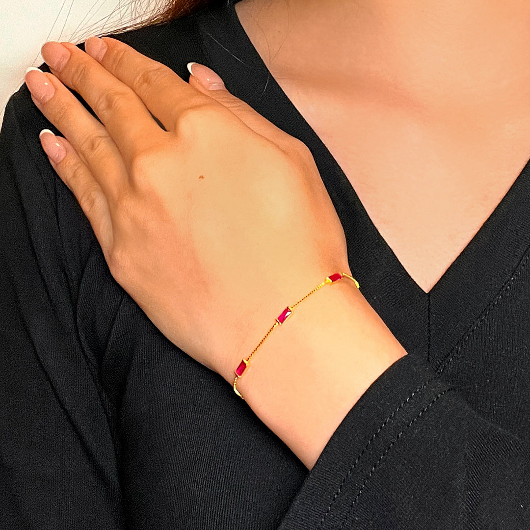 Bracelet en argent fin avec des pierres de cornaline rouge et de petites perles dorées, porté au poignet d'une femme.