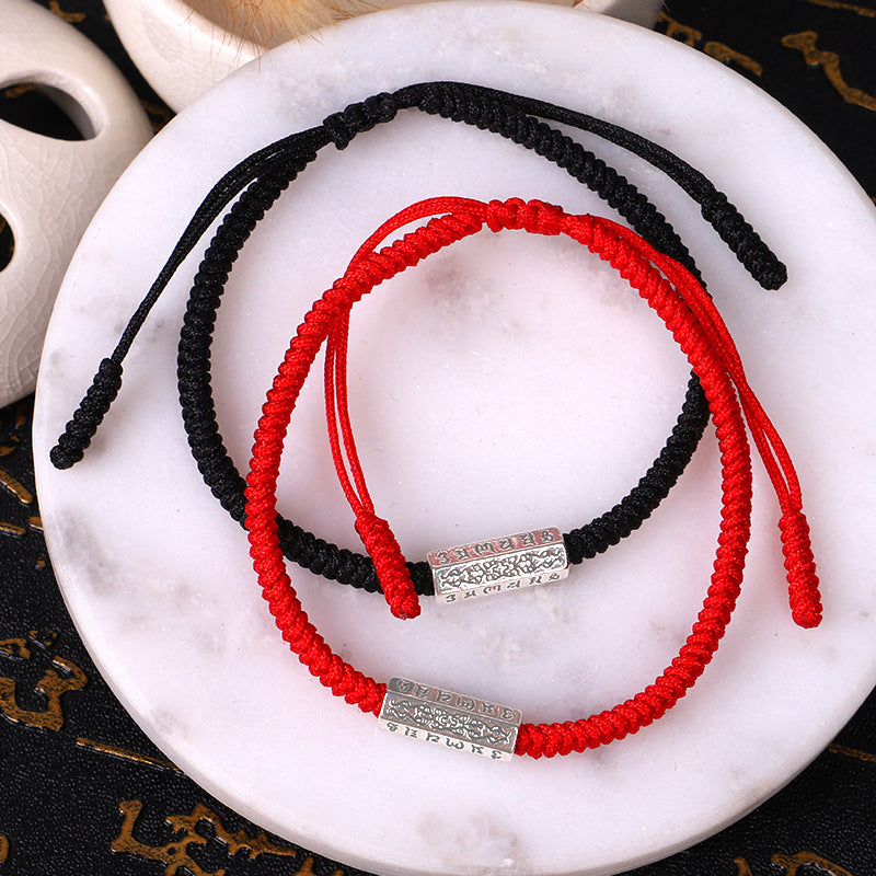 Ensemble de deux bracelets tressés, un rouge et un noir, avec une barre argentée gravée de symboles bouddhistes sur chaque bracelet.