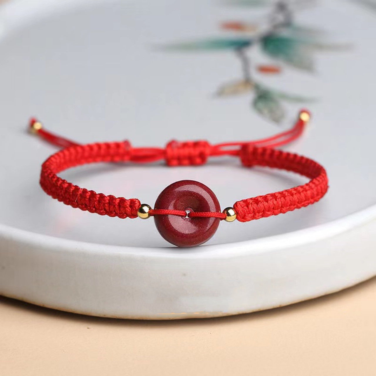 Bracelet cordon rouge avec une perle ronde rouge cinabre et deux petites perles dorées, ajustable.