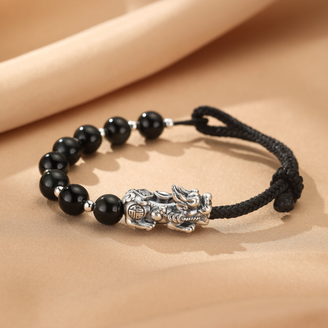 Bracelet de couple Pi Xiu en pierre d'obsidienne et fil rouge avec une breloque mythologique chinoise en argent.