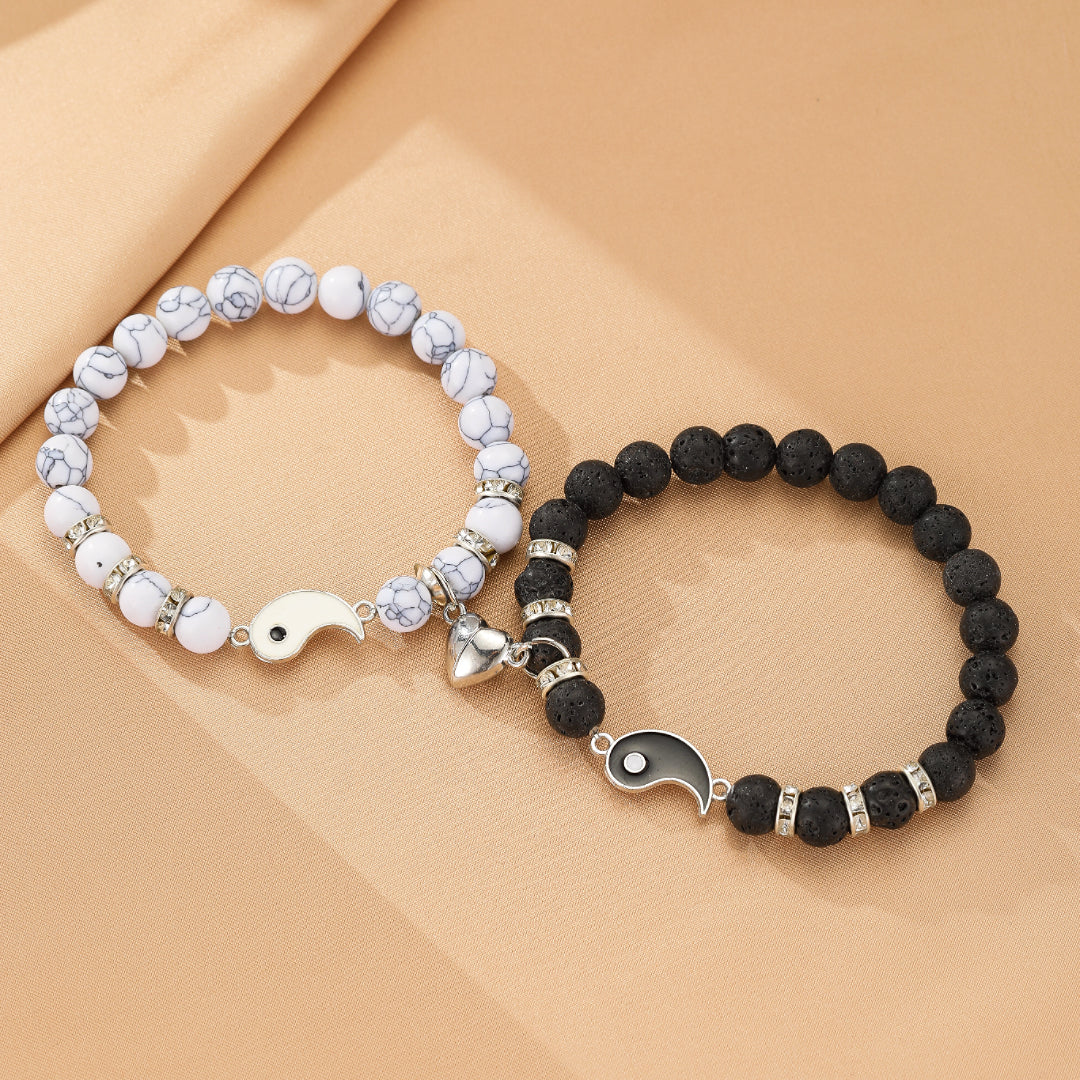 Deux bracelets assortis pour couple, l'un en pierre de lave noire et l'autre en howlite blanche, ornés d'un pendentif Yin et Yang magnétique et de perles argentées.