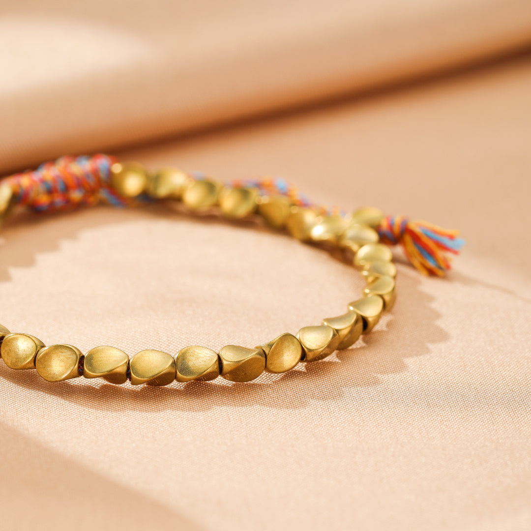 Bracelet en cuivre avec des perles dorées en forme de gouttelettes et un cordon tressé multicolore orange, bleu et rouge.