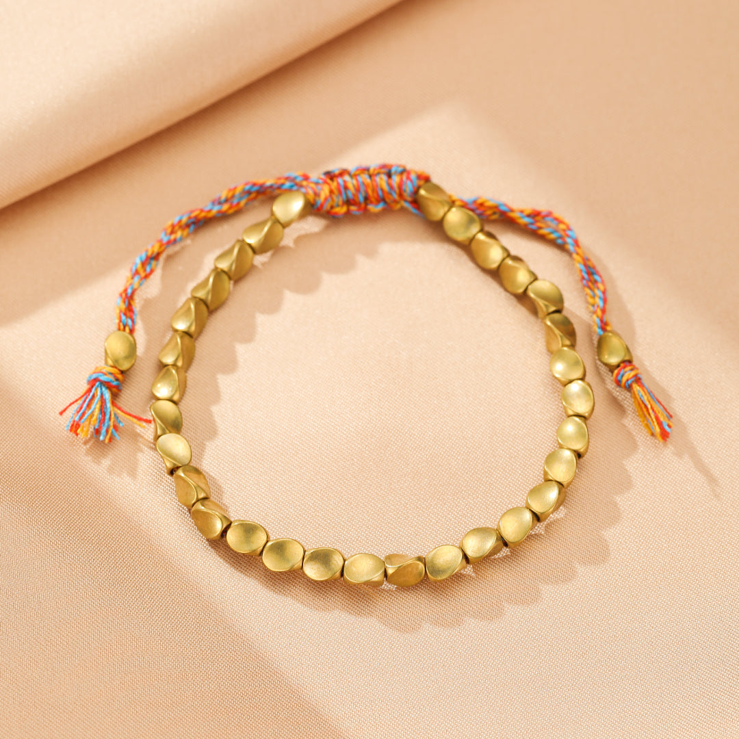 Bracelet en cuivre avec perles dorées et cordon tressé multicolore bleu, orange et rouge, fermé par un nœud coulissant.