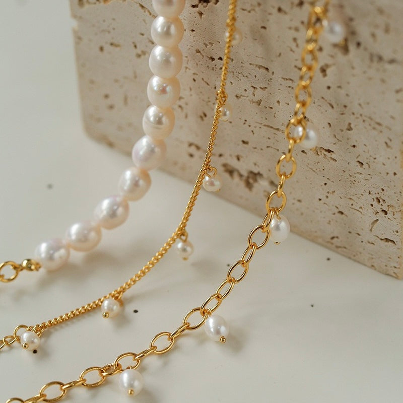 Gros plan sur deux bracelets de cheville plaqués or, l'un orné de perles blanches baroques et l'autre d'une chaîne avec de petites perles pendantes.