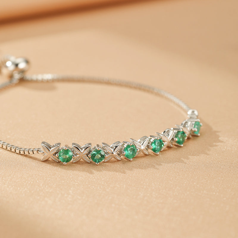 Bracelet en argent avec des motifs de X et O alternés, serti de petites pierres d'émeraude rondes et brillantes.