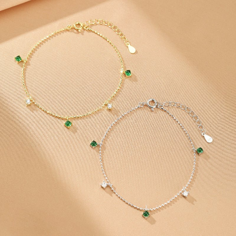 Deux bracelets délicats en argent 925, l'un doré et l'autre argenté, ornés de petites pierres d'émeraude et de cristaux cubiques, montrant leur éclat.