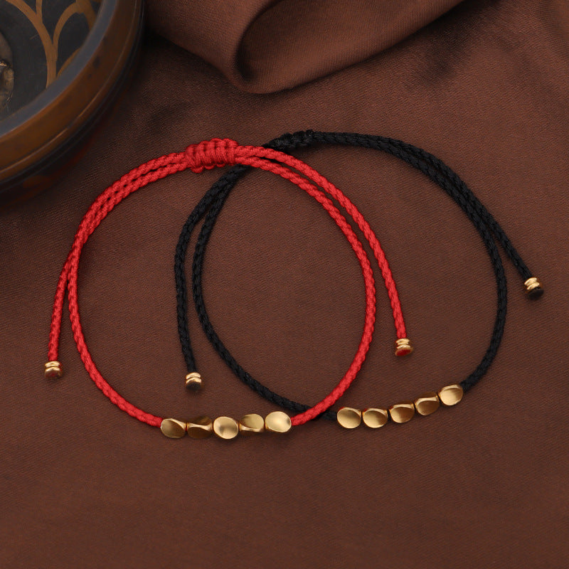 Deux bracelets en fil rouge et noir avec des perles dorées, symbolisant la lumière et la protection, sur un fond brun.
