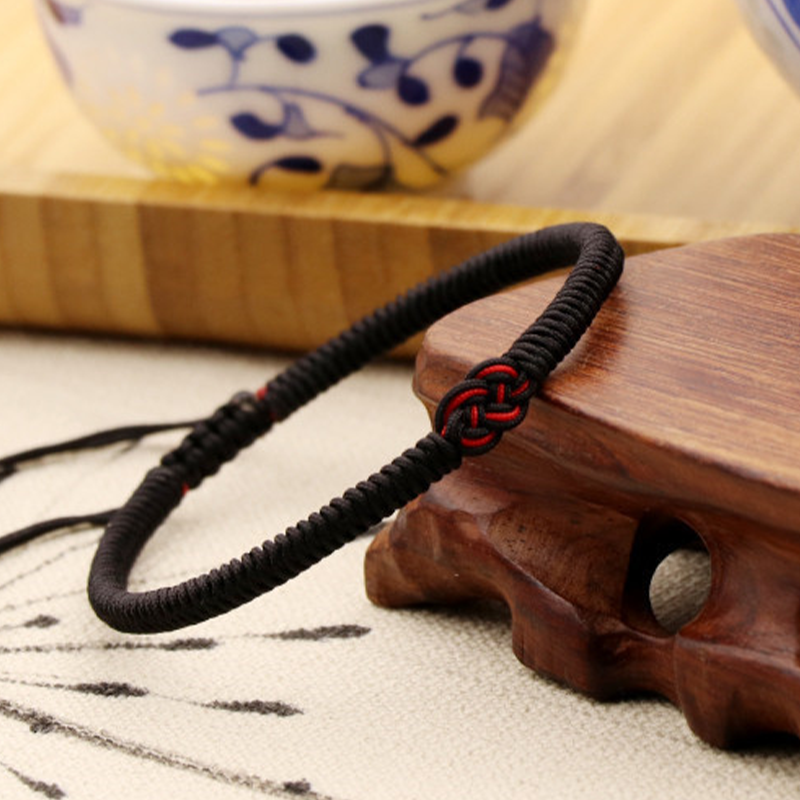 Bracelet fil rouge tressé noir avec nœud décoratif rouge, symbole de protection et de chance