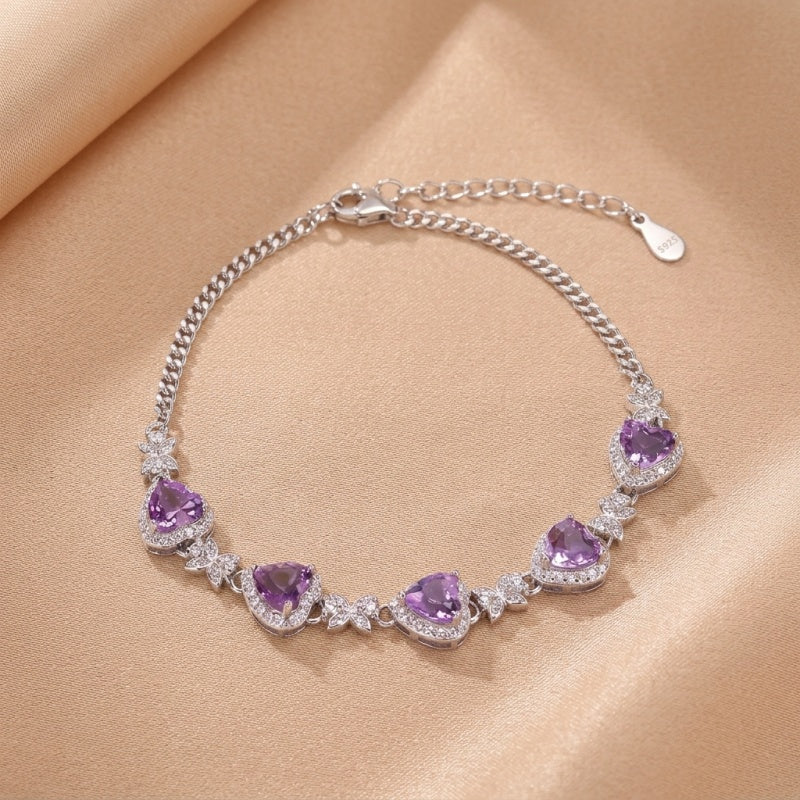 Bracelet en argent 925 avec des cœurs d'améthyste et des zircons cubiques blancs scintillants, sur un fond beige satiné.