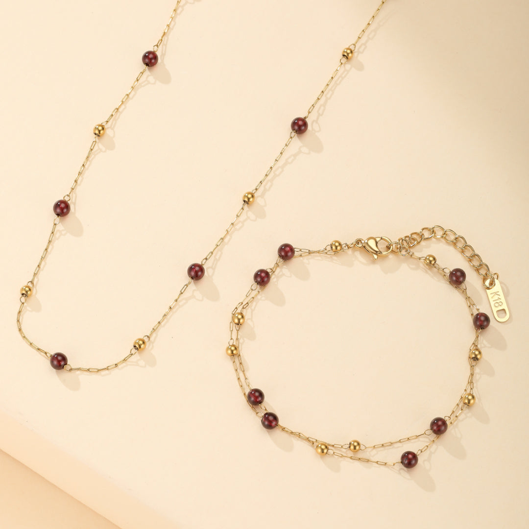 Ensemble de bijoux plaqué or 18 carats avec bracelet et collier ornés de grenats et de petites perles dorées.