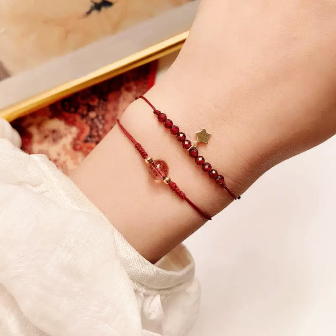 Deux bracelets fins rouges avec une pierre de grenat et une pierre de quartz fraise, le bracelet du haut est orné d'une petite étoile dorée.