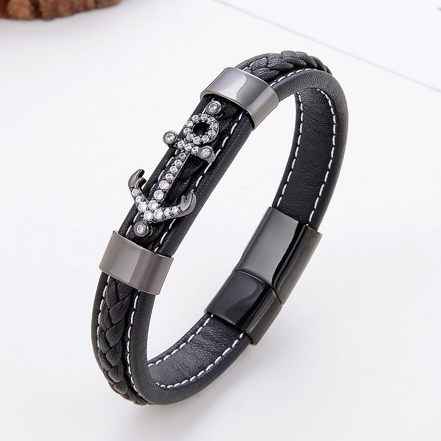 Bracelet homme en cuir tressé noir avec un fermoir magnétique noir et un pendentif ancre orné de strass brillants.