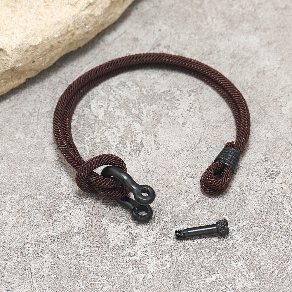Bracelet homme en corde marron avec fermoir noir et détails de cordon, sur fond texturé.
