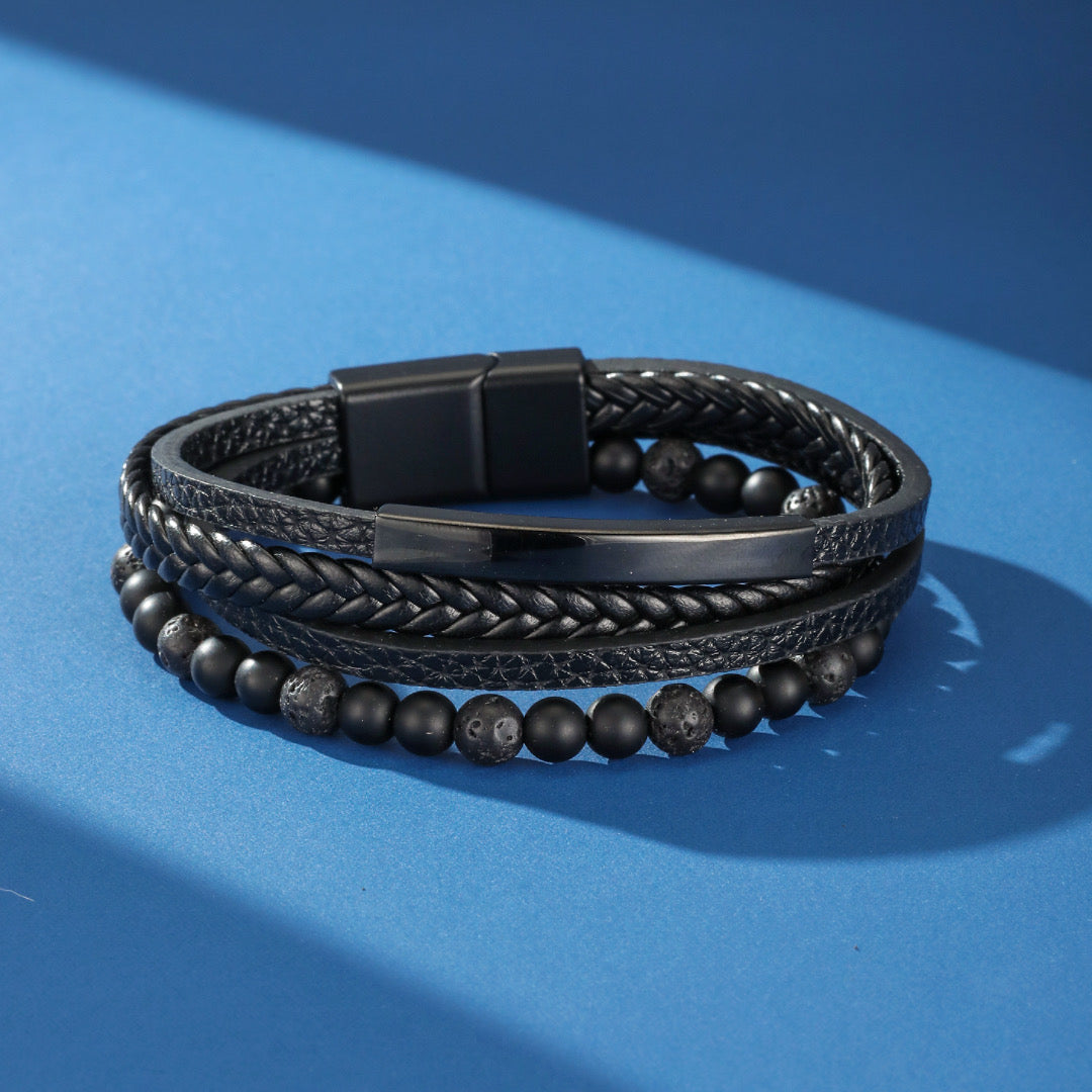 Bracelet homme multicouche en cuir noir tressé avec perles mates et perles de lave, orné d'une barre métallique et d'un fermoir magnétique.