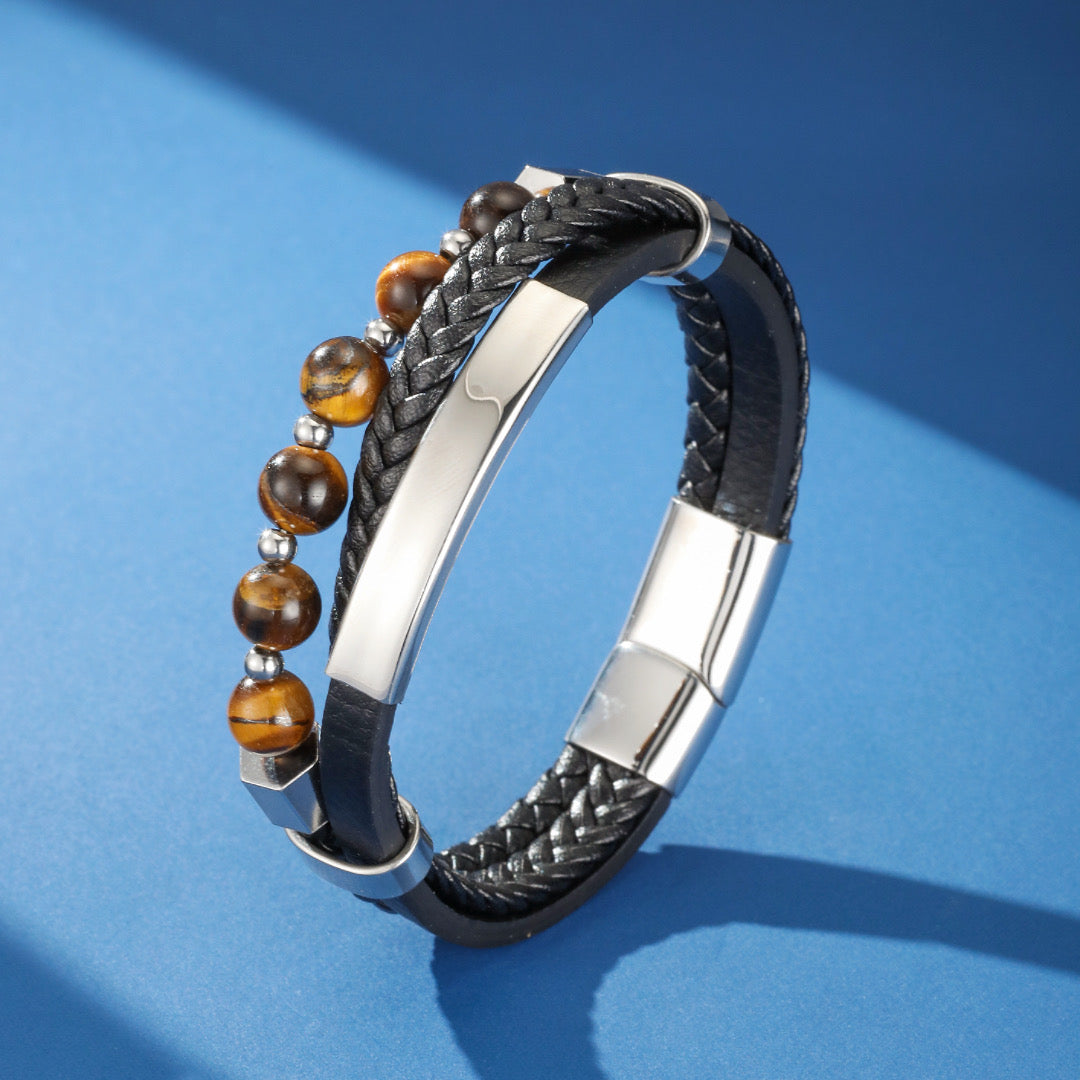 Bracelet homme en cuir tressé noir avec perles d'œil de tigre et une plaque centrale en acier inoxydable.