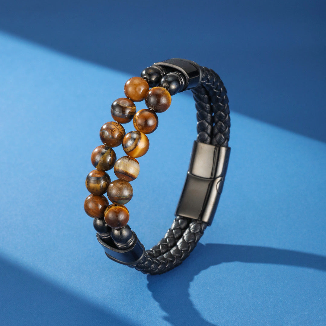 Bracelet homme double rang en cuir tressé noir avec perles naturelles d'œil de tigre et fermoir magnétique noir sur fond bleu.