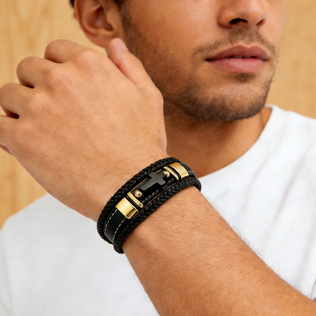 Bracelet homme en cuir noir tressé avec fermoir noir en forme de croix et détails dorés, orné de perles d'onyx, porté au poignet.