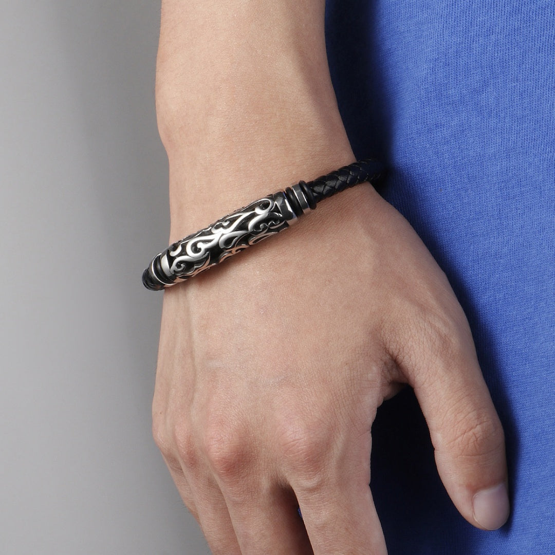 Bracelet homme en cuir tressé noir avec un fermoir orné de motifs tribaux argentés, porté au poignet.