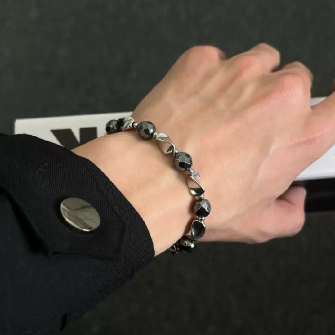 Bracelet pour homme en hématite avec des perles facettées et des éléments argentés, porté au poignet.