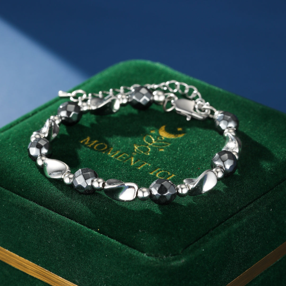 Bracelet homme en hématite avec des perles facettées et des éléments argentés, posé sur un écrin vert.