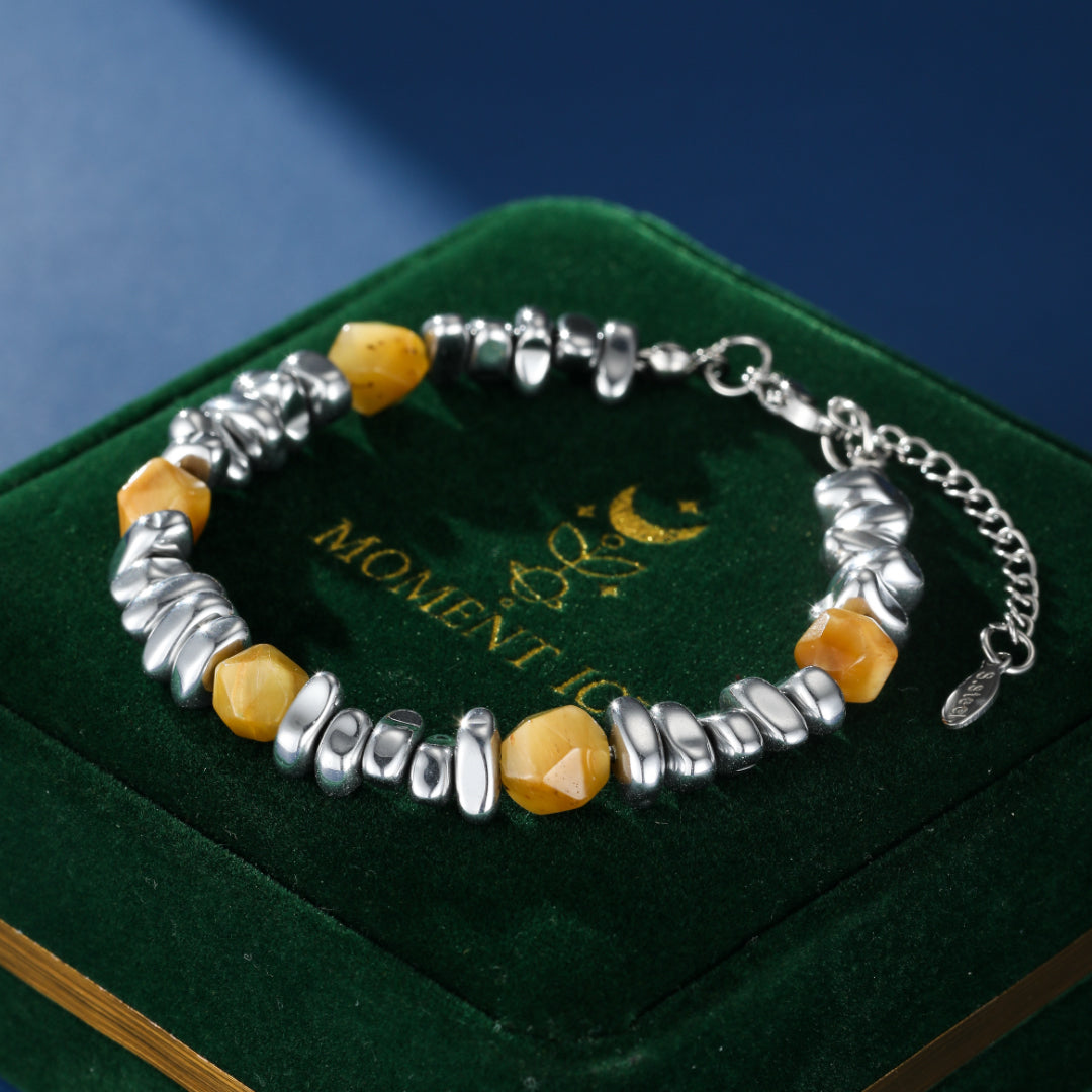Bracelet homme Prisme Minéral composé de perles irrégulières en œil de tigre jaune et d'éléments argentés, posé sur un écrin en velours vert.