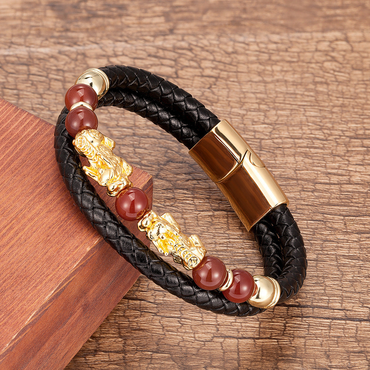 Bracelet en cuir tressé noir avec perles d'agate rouge et ornements dorés en forme de Pi Xiu, fermoir magnétique doré.