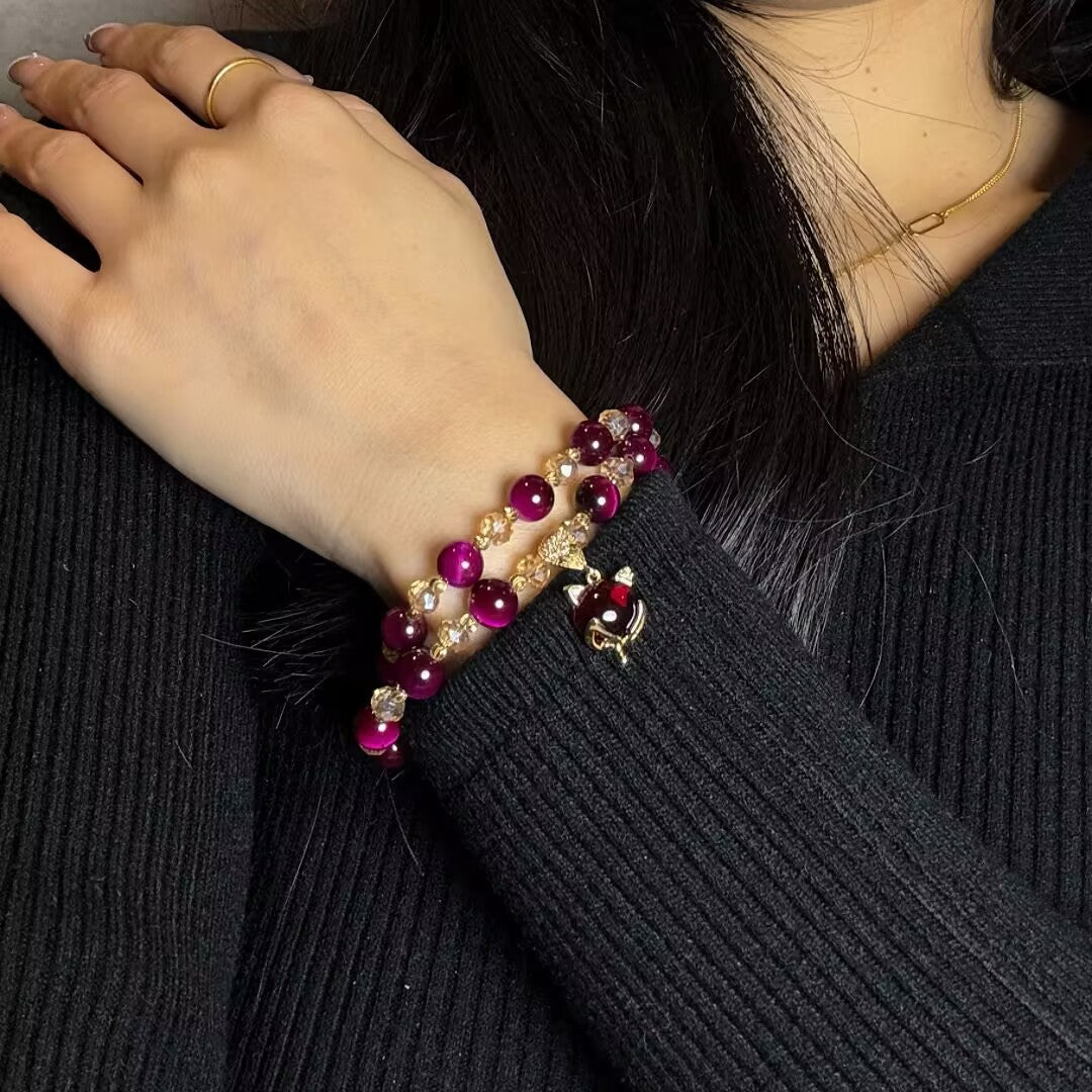 Bracelet double rang avec perles œil de tigre violettes et breloque chat dorée, porté au poignet d'une femme