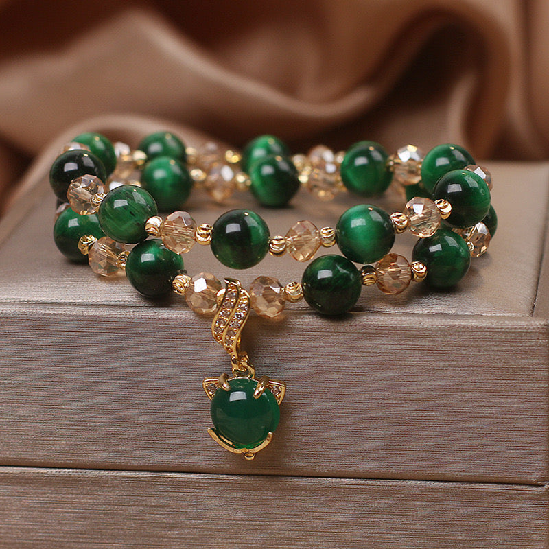 Bracelet double rang en œil de tigre vert, agrémenté d'un pendentif breloque en forme de tête de chat stylisée, orné de pierres scintillantes et de perles dorées.
