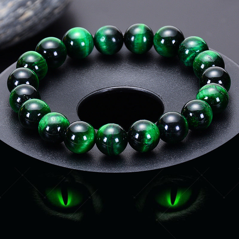 Bracelet en œil de tigre vert, avec des perles polies rondes, le bracelet est posé sur un support noir avec un reflet de chat aux yeux verts.