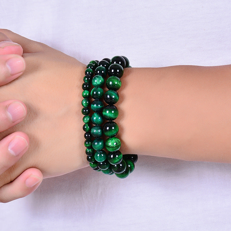 Plusieurs bracelets faits de perles rondes vertes d'œil de tigre de tailles variées, portés sur un poignet.