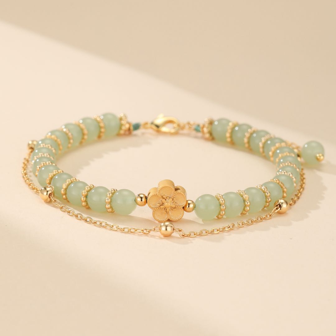 Bracelet double rang avec perles de jade vert pâle et un pendentif fleur dorée au centre, chaîne dorée fine.