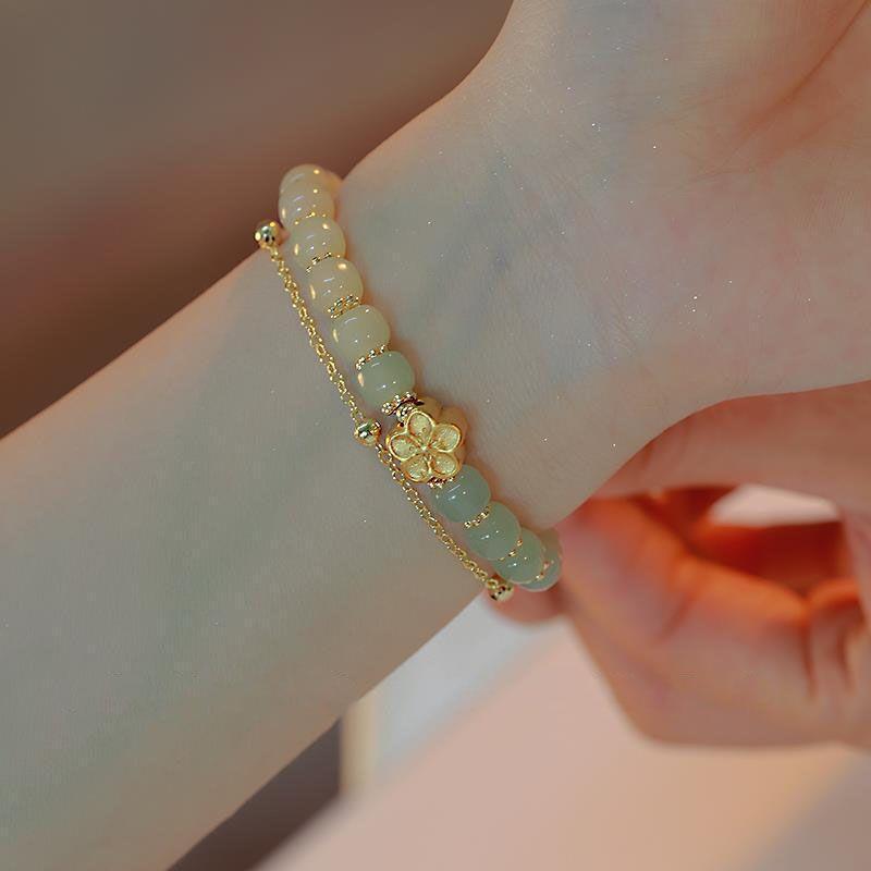 Bracelet "Caresse de Sakura" en jade avec un pendentif fleur doré sur un poignet