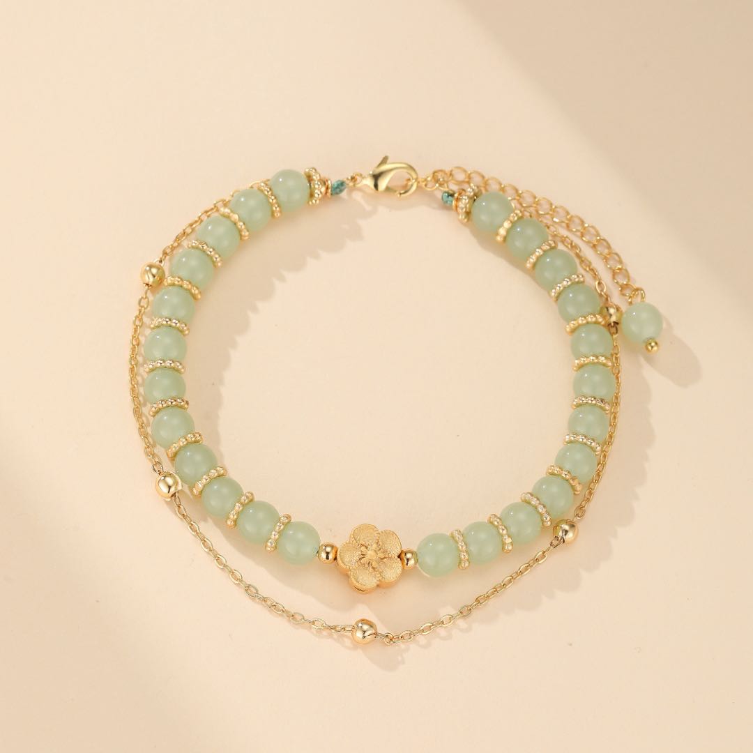 Bracelet double chaîne en jade vert pâle avec un fermoir doré et un pendentif fleur délicat.