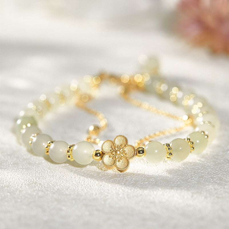Bracelet délicat en jade blanc avec un fermoir en forme de fleur dorée, orné de petites perles dorées entre chaque pierre.