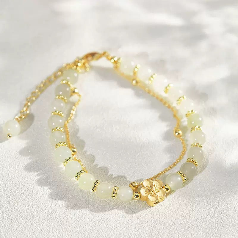 Bracelet double rang avec perles de jade vert pâle et breloque fleur dorée, style délicat et élégant.