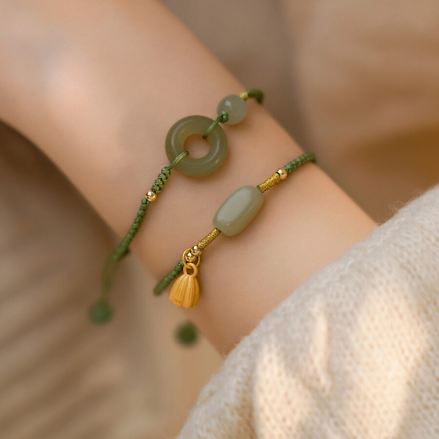 Bracelet en jade avec breloque fleur de lotus dorée et perles, sur un poignet.