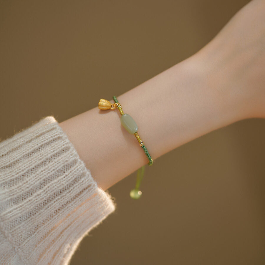 Bracelet en jade avec une perle ovale verte et un pendentif doré en forme de lotus, porté au poignet.