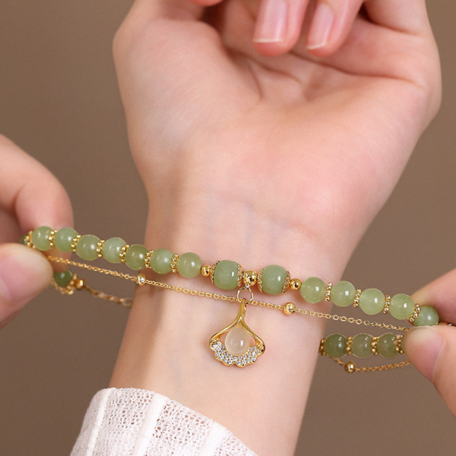 Bracelet en jade avec un pendentif feuille de ginkgo plaqué or et serti de zircons blancs sur un poignet.