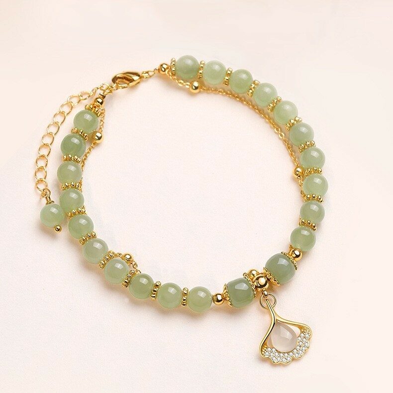 Bracelet double rang avec des perles de jade vert pâle et un pendentif feuille de ginkgo orné de zirconiums, monté sur une chaîne plaqué or.