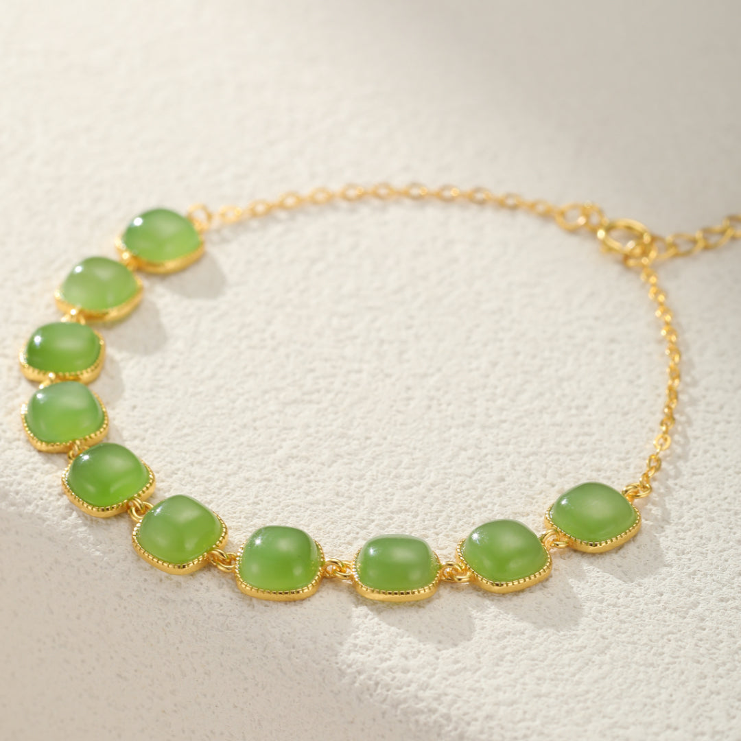 Bracelet en jade avec des pierres vertes carrées et une chaîne plaquée or, détail de bijou lumineux.