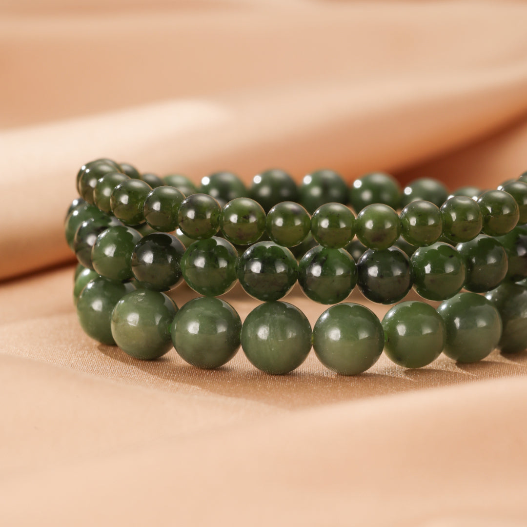 Trois bracelets en perles de jade vert, empilés les uns sur les autres, sur un fond de tissu beige.