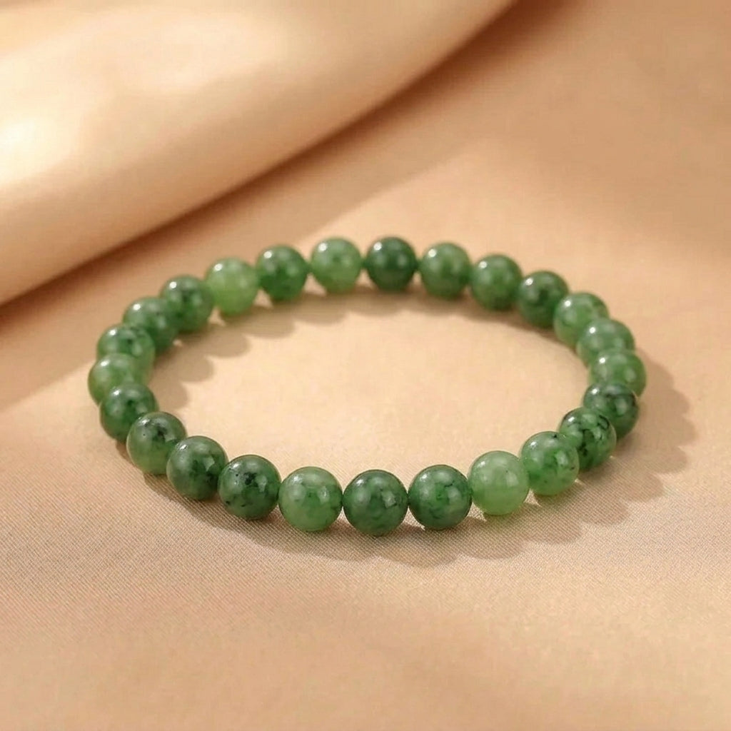 Bracelet de perles en jade vert naturel Source Secrète posé sur un fond en tissu satiné beige