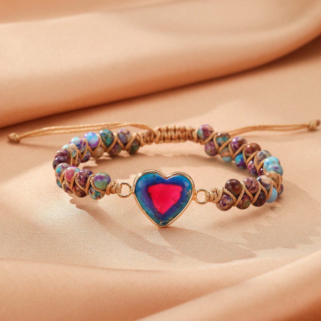 Bracelet Jaspe avec un pendentif en forme de cœur bleu et rose, entouré de perles multicolores et d'un cordon tressé.