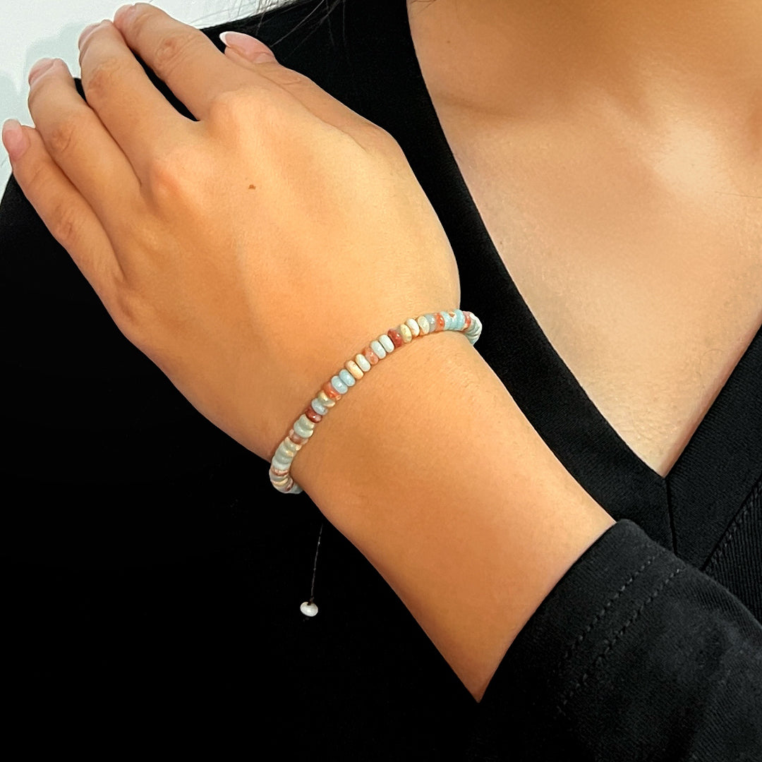 Bracelet en jaspe aux couleurs douces, bleu pâle, beige et corail, avec une fine chaîne réglable et une perle blanche.