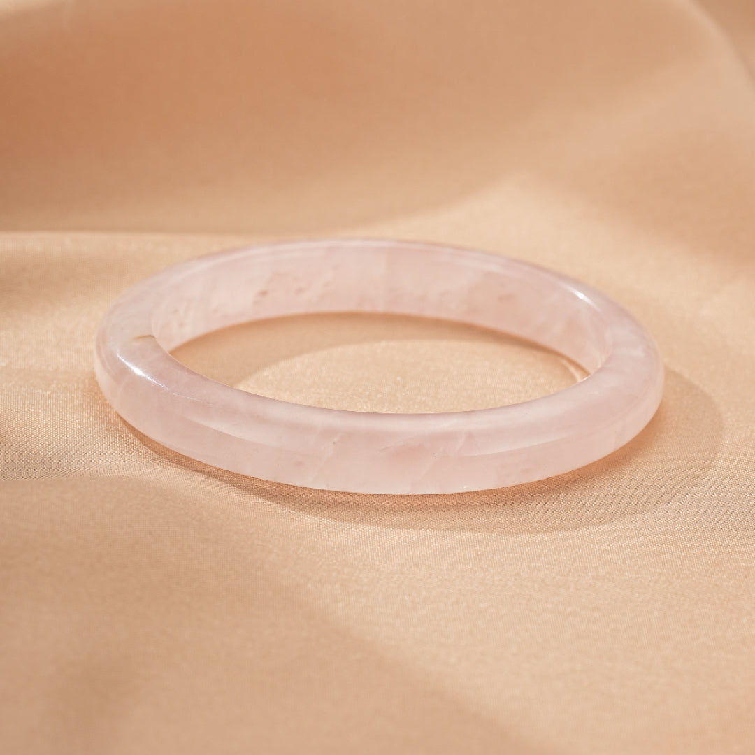 Bracelet jonc en quartz rose naturel, d'une teinte rose pâle douce, posé sur un tissu satiné beige.
