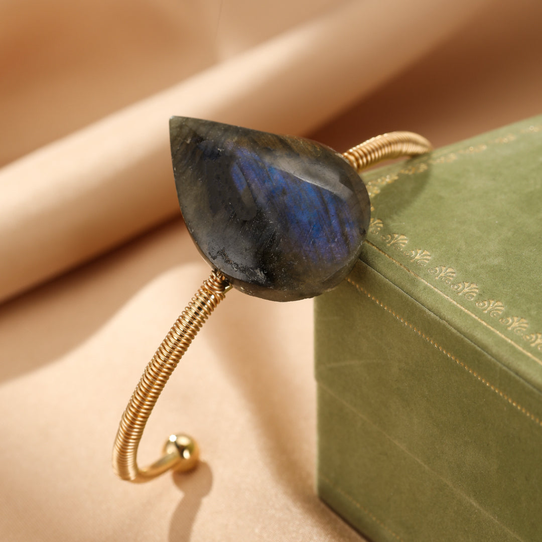 Bracelet jonc en laiton doré avec une grosse pierre de labradorite aux reflets bleus et violets, en forme de goutte.