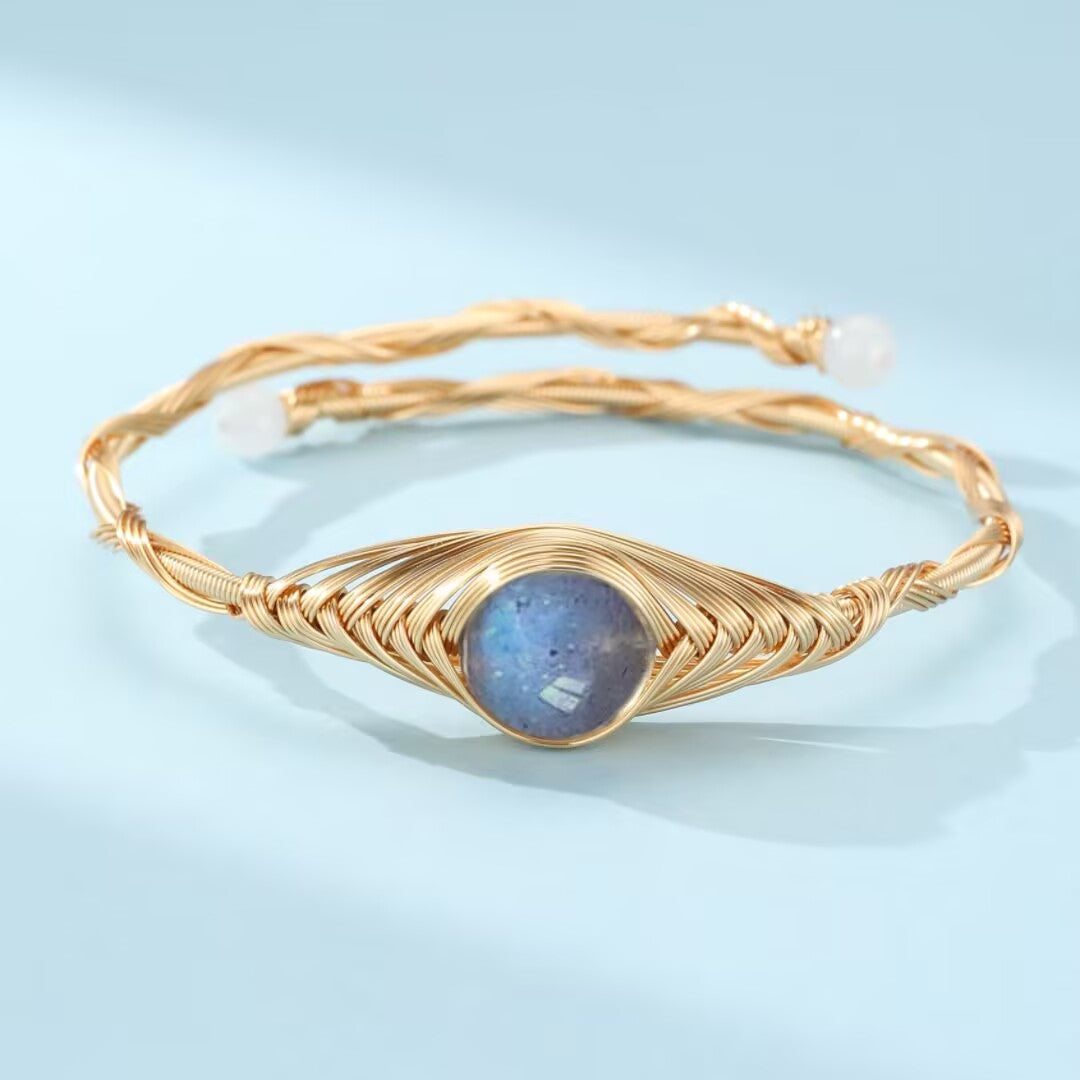 Bracelet jonc ajustable en fil doré torsadé avec une pierre centrale de labradorite bleue irisée et deux petites perles blanches aux extrémités.