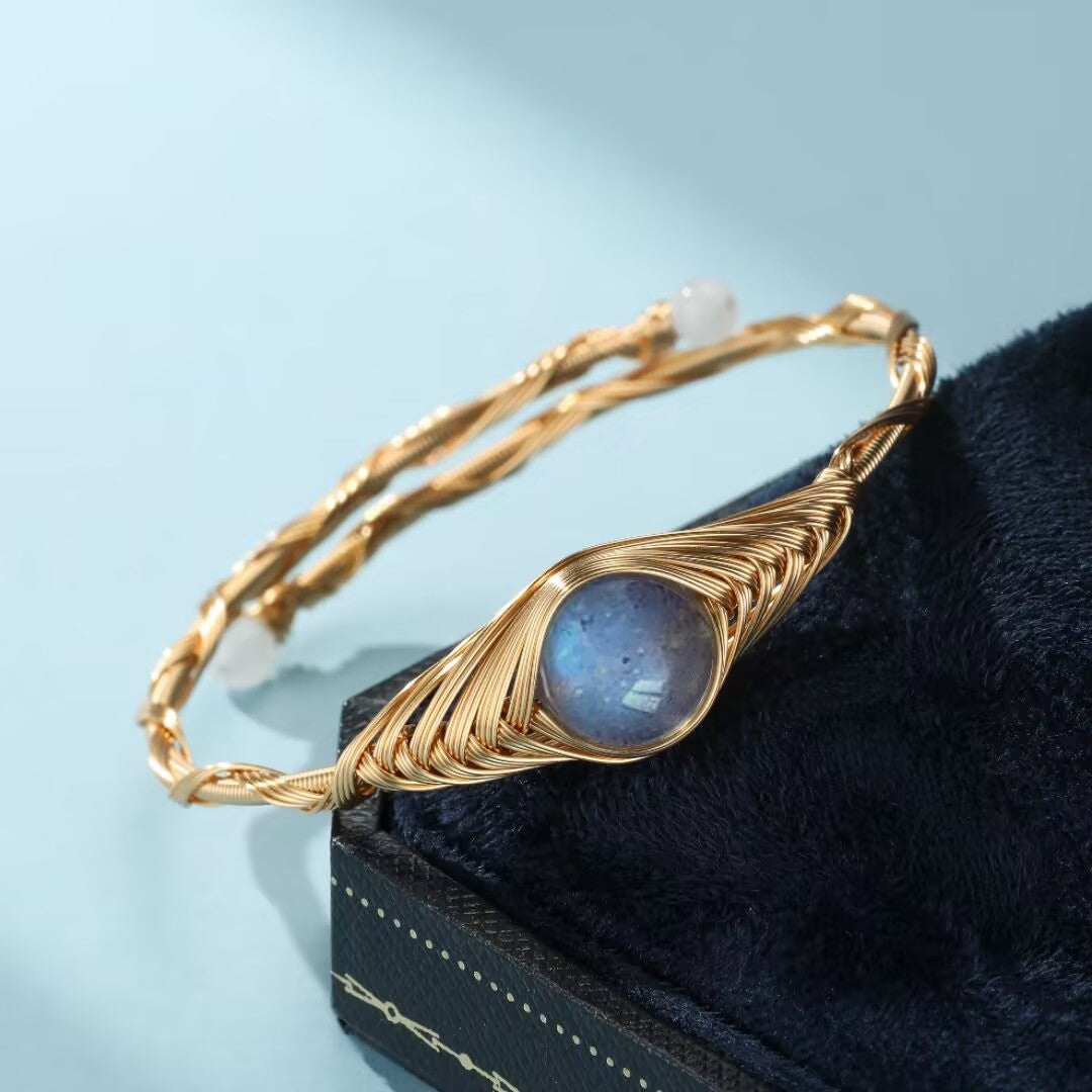 Bracelet jonc en fil doré torsadé serti d'une pierre de labradorite bleue au centre, orné de deux petites perles blanches aux extrémités.