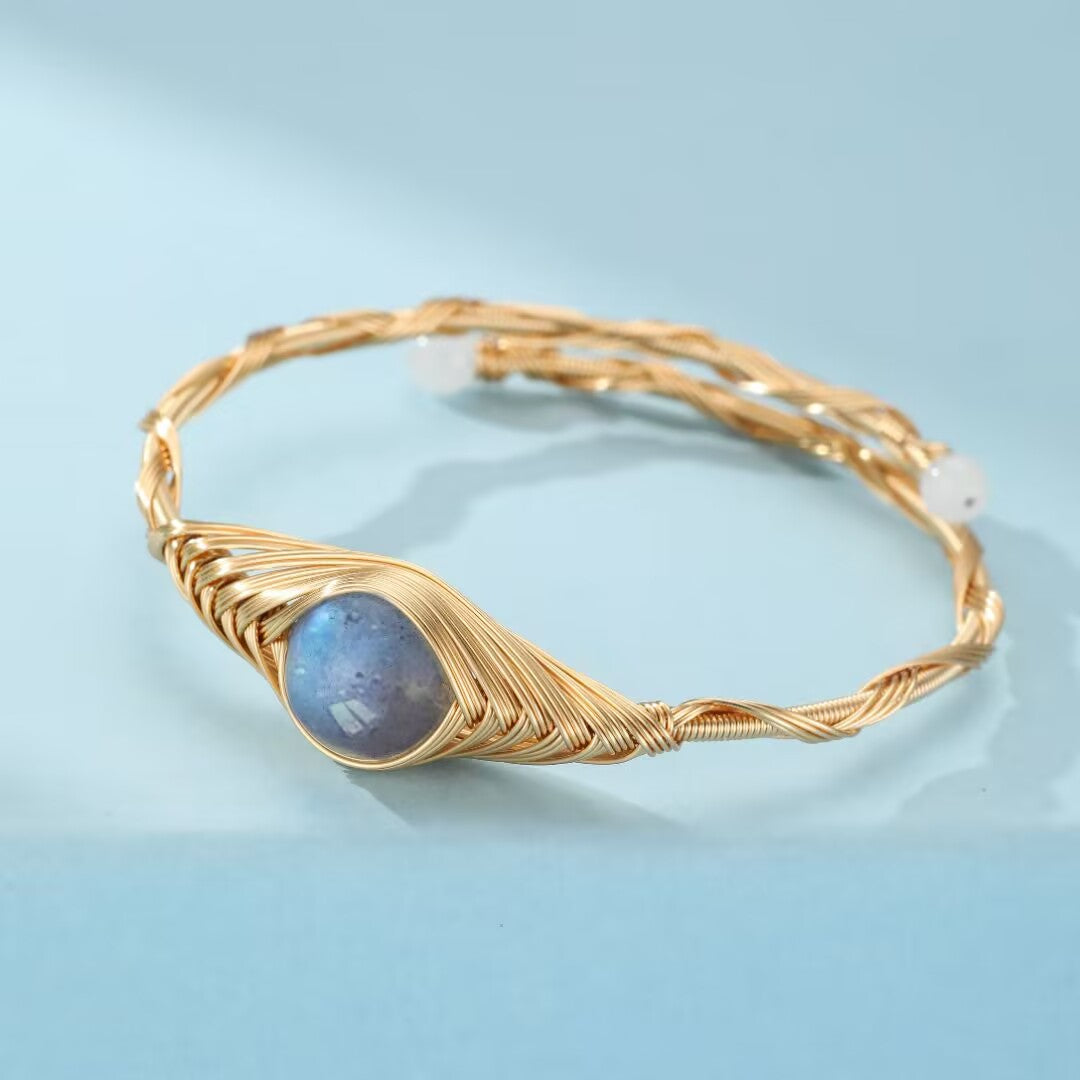 Bracelet en fil doré torsadé avec une pierre de labradorite bleue au centre et deux petites perles blanches de chaque côté, style bohème.