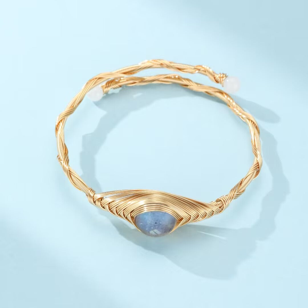 Bracelet en fil doré torsadé avec une pierre de labradorite bleue au centre, rappelant le troisième œil.